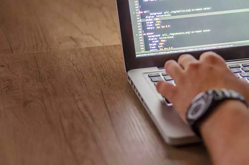 Person's hand on a laptop with code on the screen