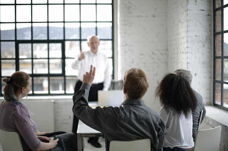 Teacher in front of a class while student raises hand asking question