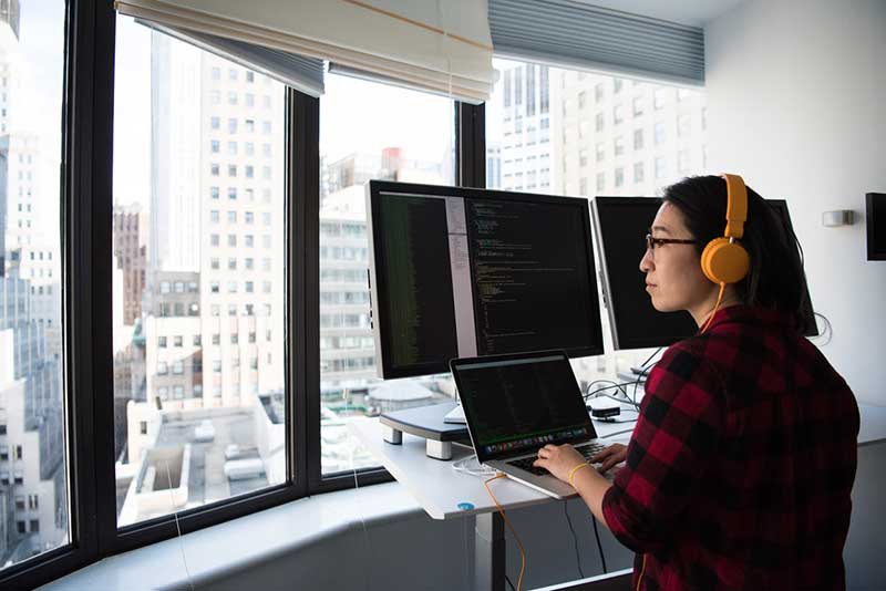 Woman coding and working from home while looking out a window onto a city
