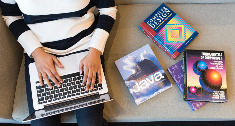 Woman on laptop with coding language books